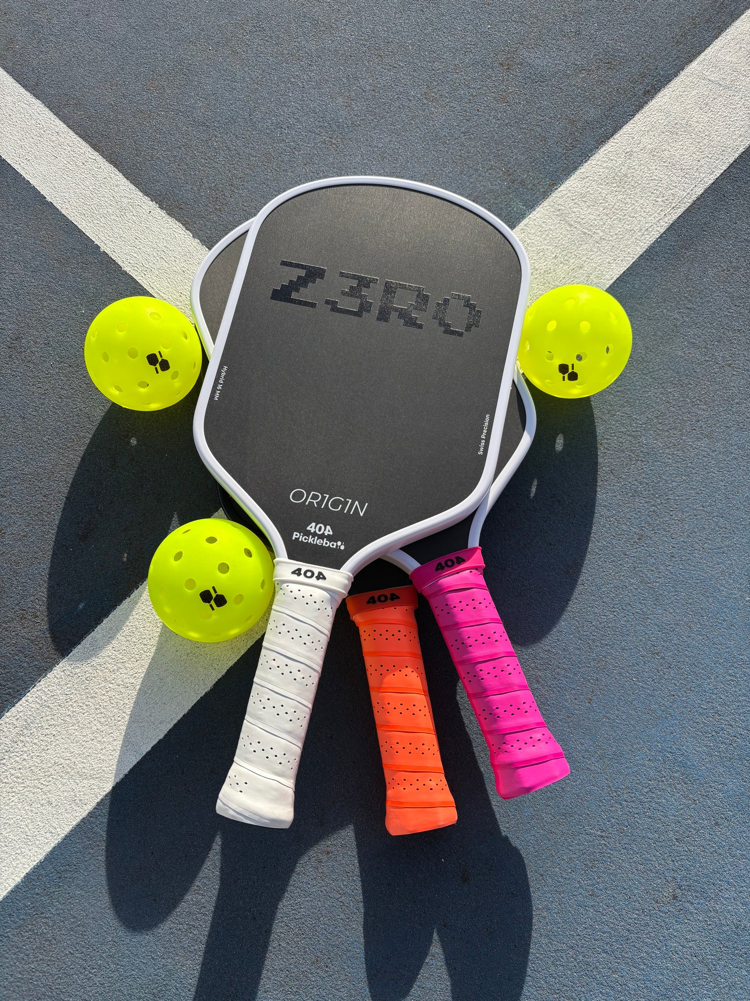 Three pickleball paddles with colorful handles on a court surface.